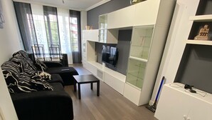 Una sala de estar moderna con un sofá negro, una mesa de centro y un televisor montado en un mueble blanco.
