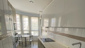 Una cocina moderna con armarios blancos, un lavamanos de acero inoxidable y un comedor con mesa y sillas.