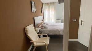 Una habitación de hotel con cama, una silla, una mesita de noche y una puerta.