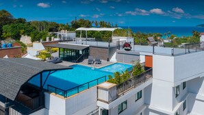 A rooftop pool with a glass barrier, lounge chairs, and a view of the ocean. - KK - Karon Kata Boutique Hotel (Karon)