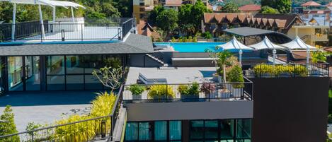 Un hotel moderno con piscina en la azotea, balcones de vidrio y vistas de las colinas circundantes.