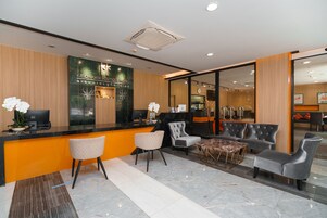 A modern hotel reception area with a black reception desk, comfortable seating, and a large mirror reflecting the interior.