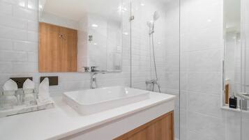 A modern bathroom with a white sink, wooden cabinet, and a glass-enclosed shower area.