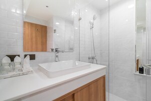 Un baño moderno con un lavamanos blanco, un armario de madera y una zona de ducha con paredes de vidrio.