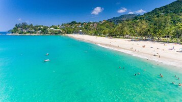 A beach with clear turquoise water, a sandy shore, and a hillside with buildings.