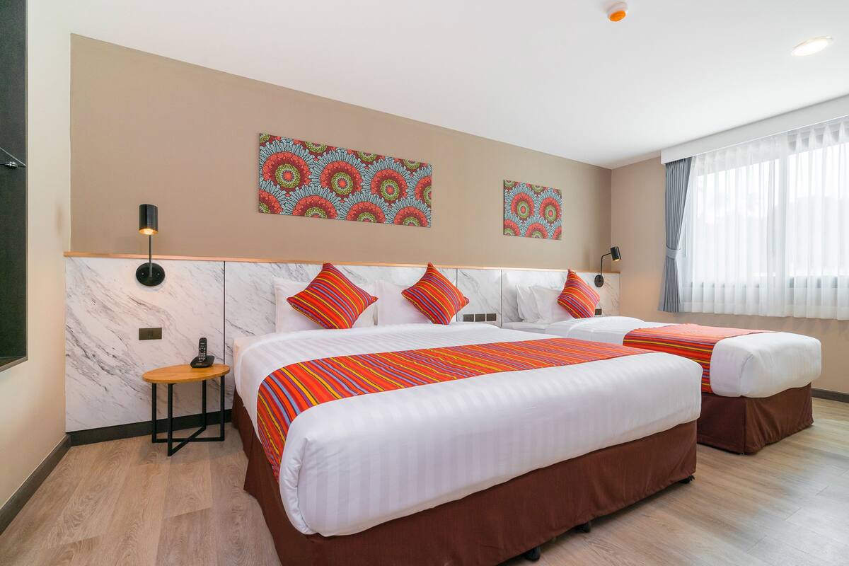 A hotel room with two beds, a marble wall, a small table with a phone, and artwork on the wall.
