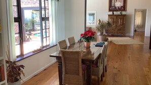 Een eetruimte met een houten tafel, rieten stoelen, een bloempot en uitzicht op het landschap door een groot raam.