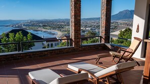 Een balkon met twee houten lounge fauteuils en uitzicht op een strand en stadsbeeld.
