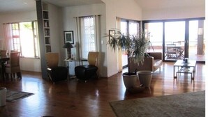 Een ruime woonkamer met houten vloeren, een grote potplant en een eethoek met een tafel en stoelen.