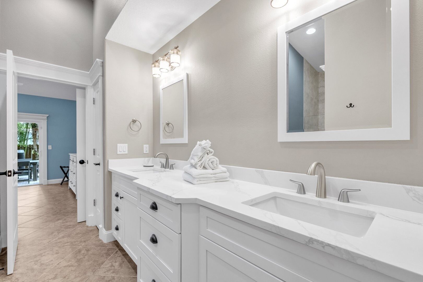 Un baño moderno con lavamanos doble, muebles blancos, un espejo grande y un perchero para toallas.