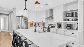 Una cocina moderna con armarios blancos, electrodomésticos de acero inoxidable e iluminación colgante.