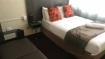 Ein Hotelzimmer mit einem Bett, einem Nachttisch, einer Lampe und einem Fenster.