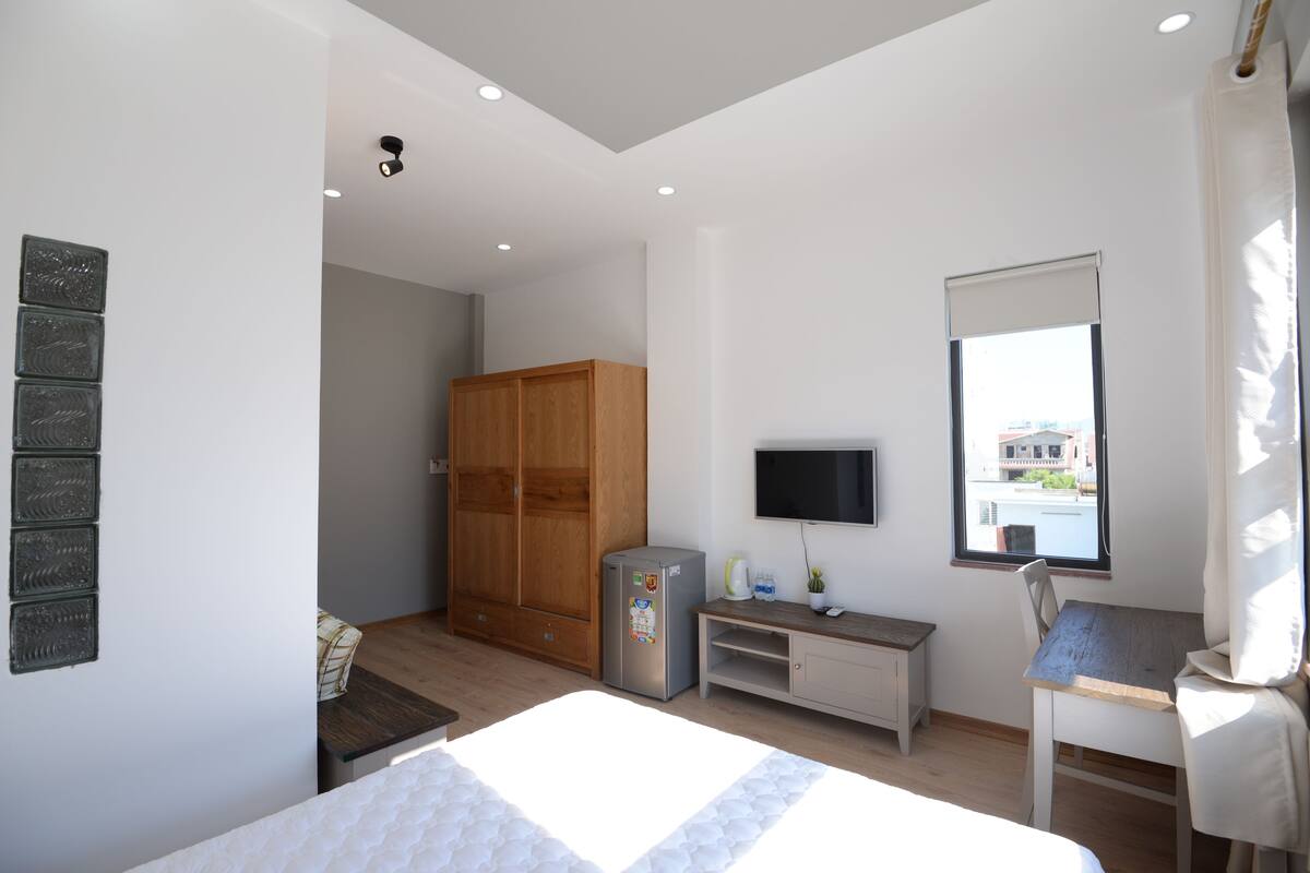 Habitación de hotel con cama, escritorio, televisor, armario y ventana con vistas.