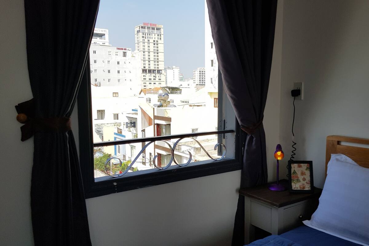 Un dormitorio con cama, mesita de noche, lámpara y ventana con cortinas.