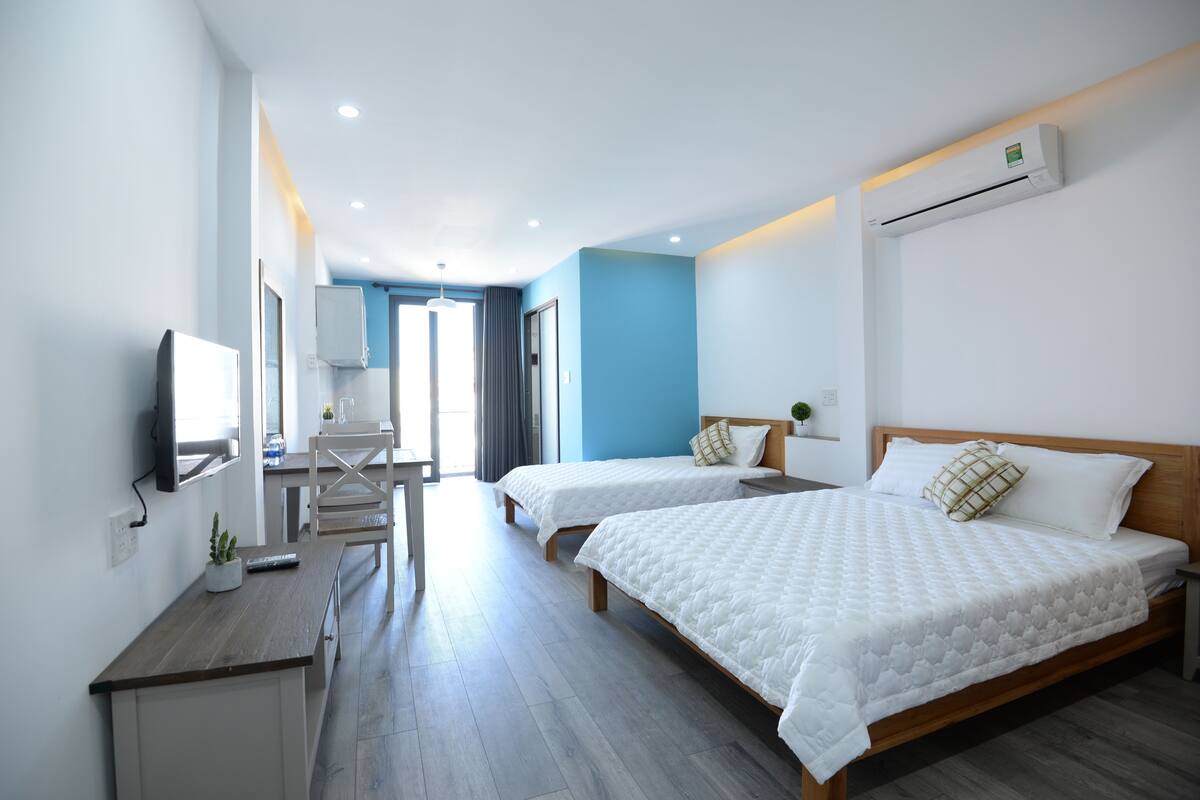 Habitación de hotel con dos camas, un escritorio, un televisor y un baño visible a través de una puerta abierta.