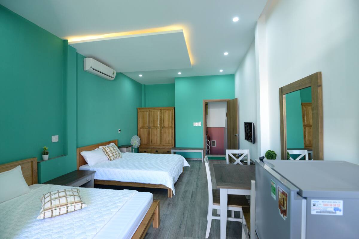Habitación de hotel con dos camas, un escritorio, una silla, un refrigerador, aire acondicionado y un espejo.