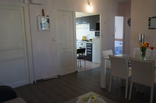 Una sala de estar con comedor, una cocina al fondo y una puerta que da a otra habitación.