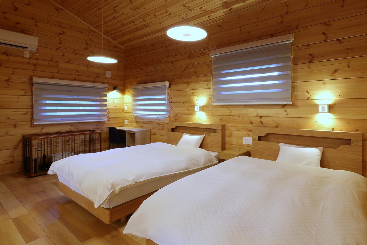 Habitación tipo cabaña con dos camas, paredes de madera e iluminación empotrada en el techo.