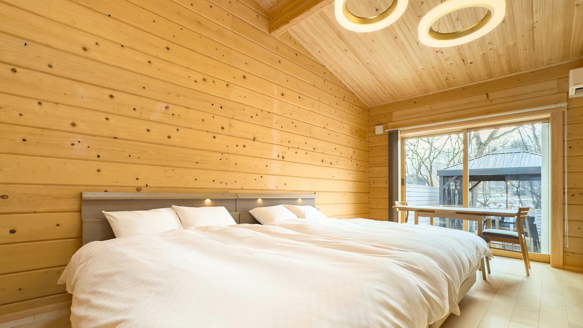 Un dormitorio de cabaña de madera con una cama, un banco junto a la ventana y vistas al exterior.