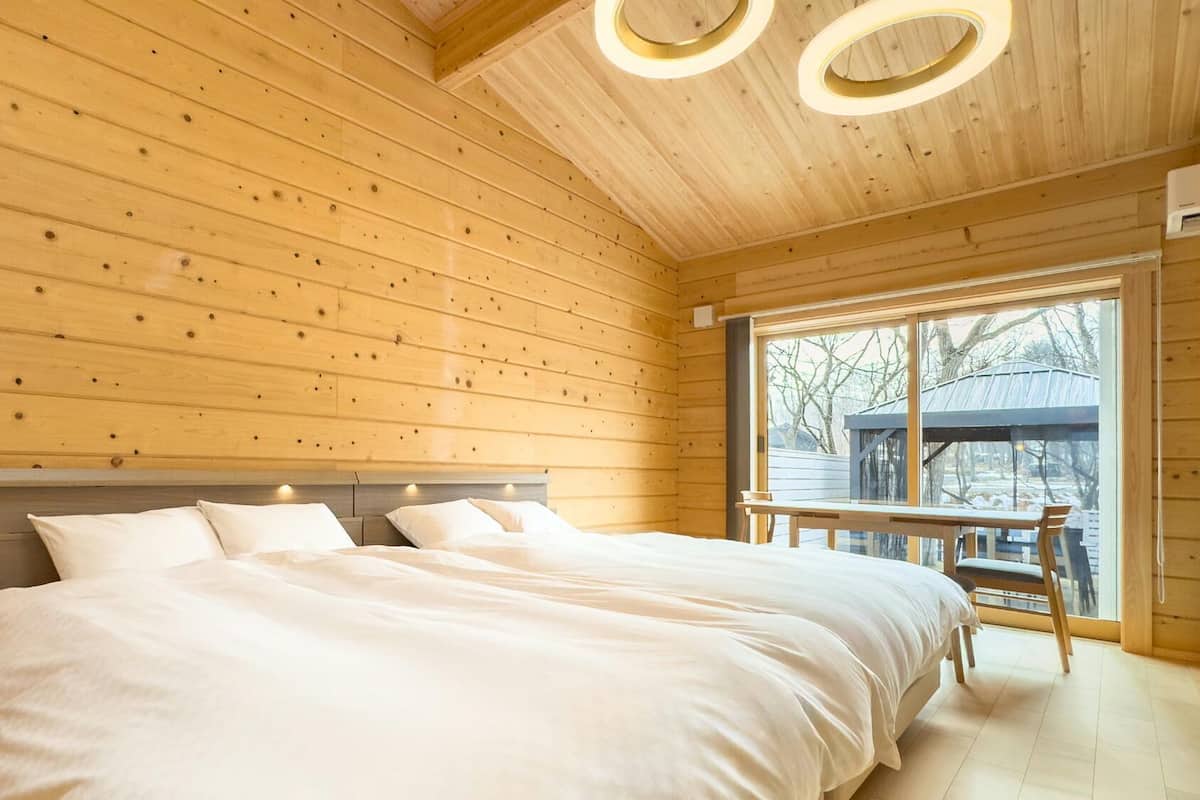 A wooden cabin bedroom with a bed, a bench by the window, and a view of the outside.