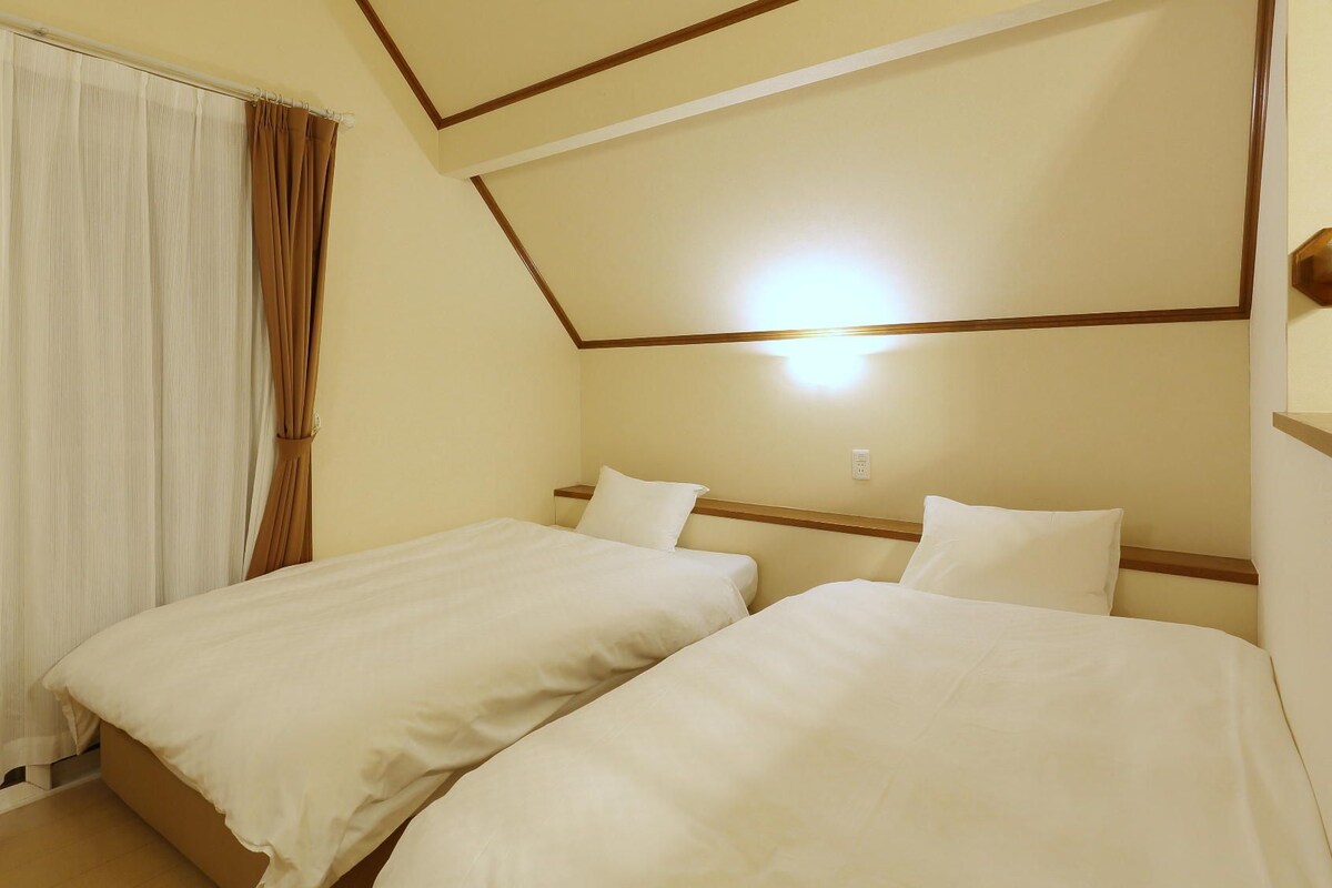 Habitación de hotel con dos camas, una ventana con cortinas y un cabecero de madera.