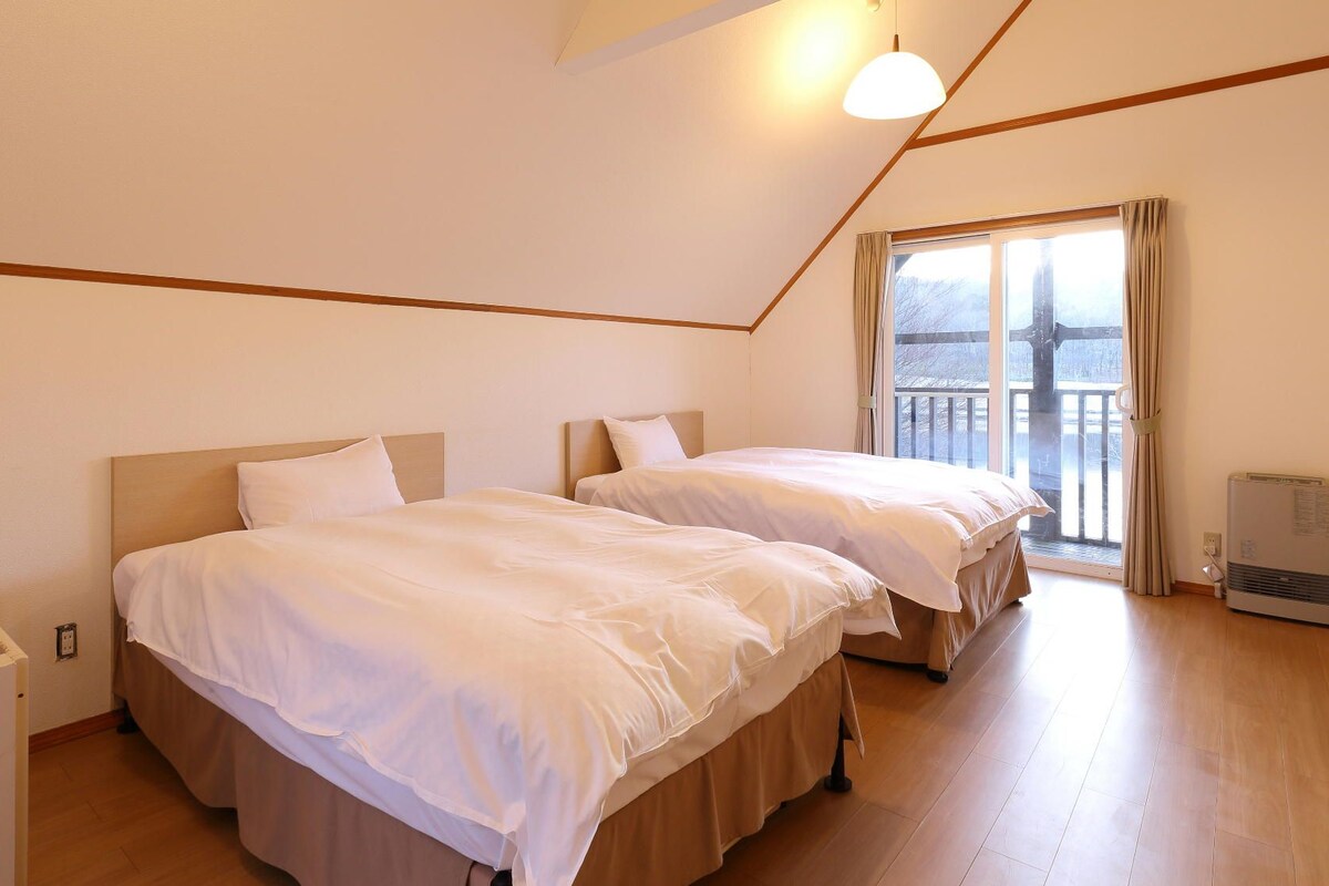 Un dormitorio con dos camas, una ventana con cortinas, un radiador y una lámpara de techo blanca.