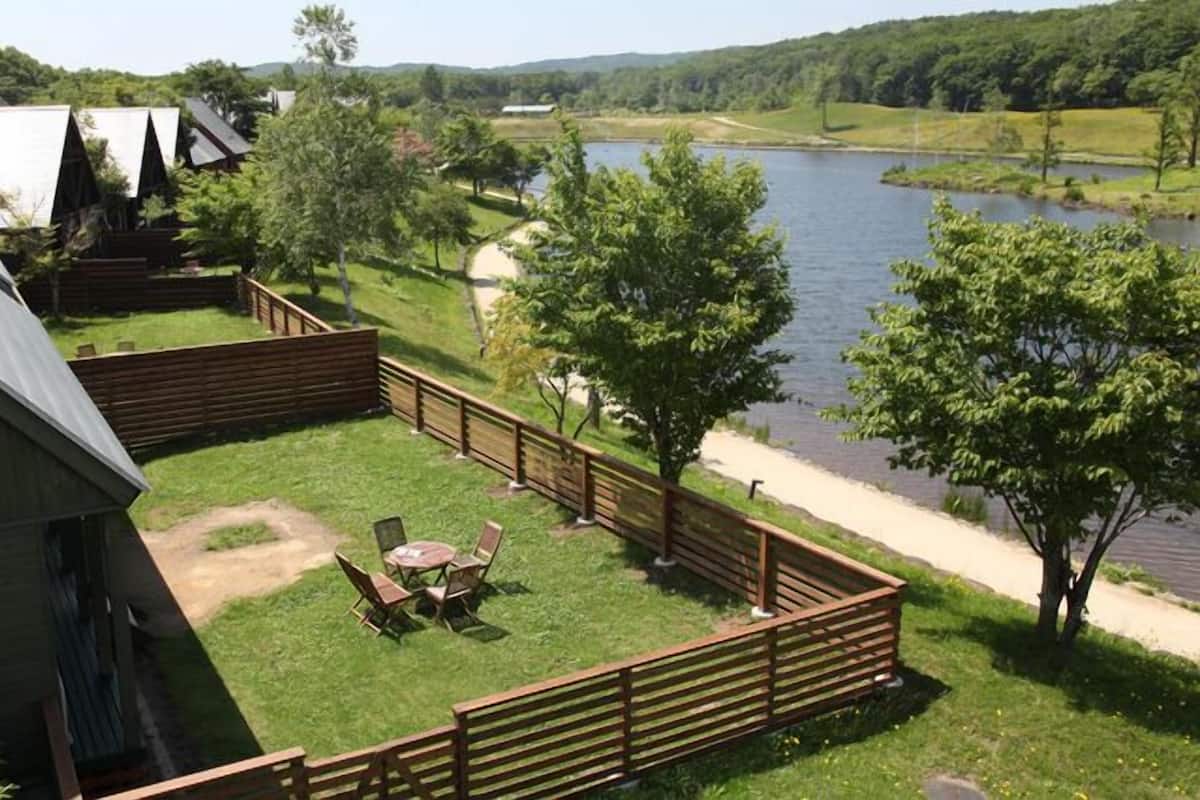 A fenced outdoor area with a picnic table and chairs, a wooden deck, and a view of a lake.