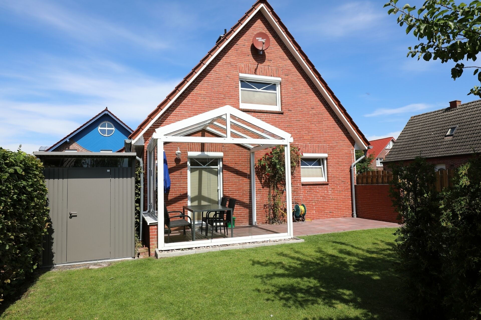 A house with a brick exterior, a covered patio with a table and chairs, and a garage.