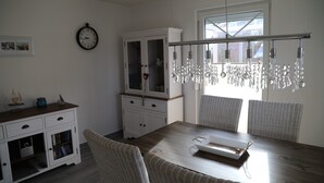 Un comedor con una mesa de madera, sillas de mimbre, un armario blanco con puertas de cristal y un reloj de pared.