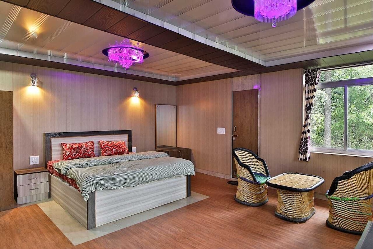 A bedroom with a bed, bedside tables, a chandelier, and a window with a view of greenery.