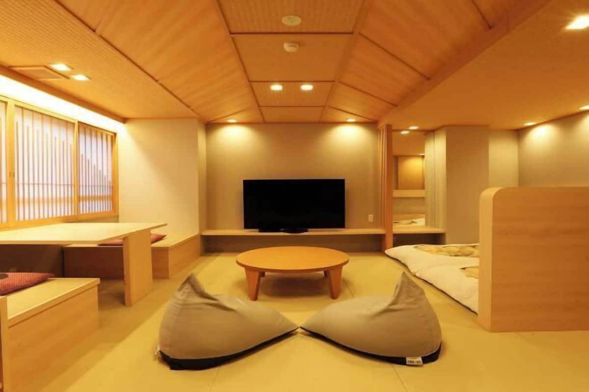 A room with a television, a round table, bean bags, and wooden furniture.