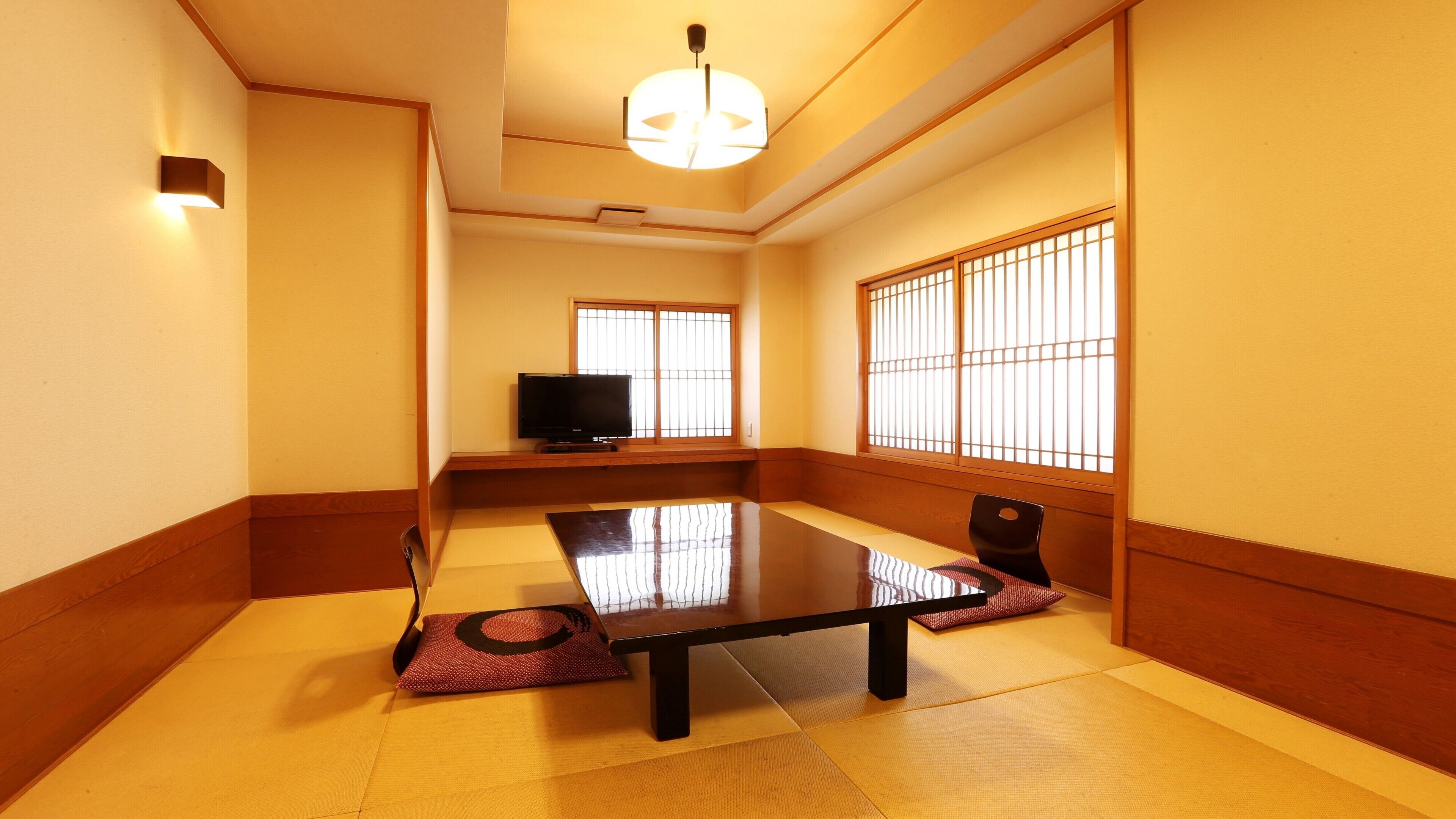 A traditional Japanese room with tatami flooring, a low table, a television, and sliding shoji doors.