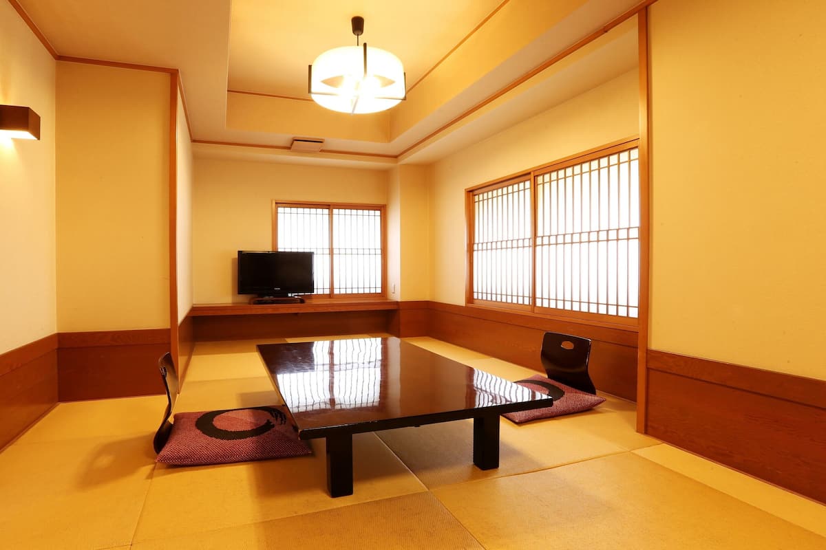 A traditional Japanese room with tatami flooring, a low table, a television, and sliding shoji doors.