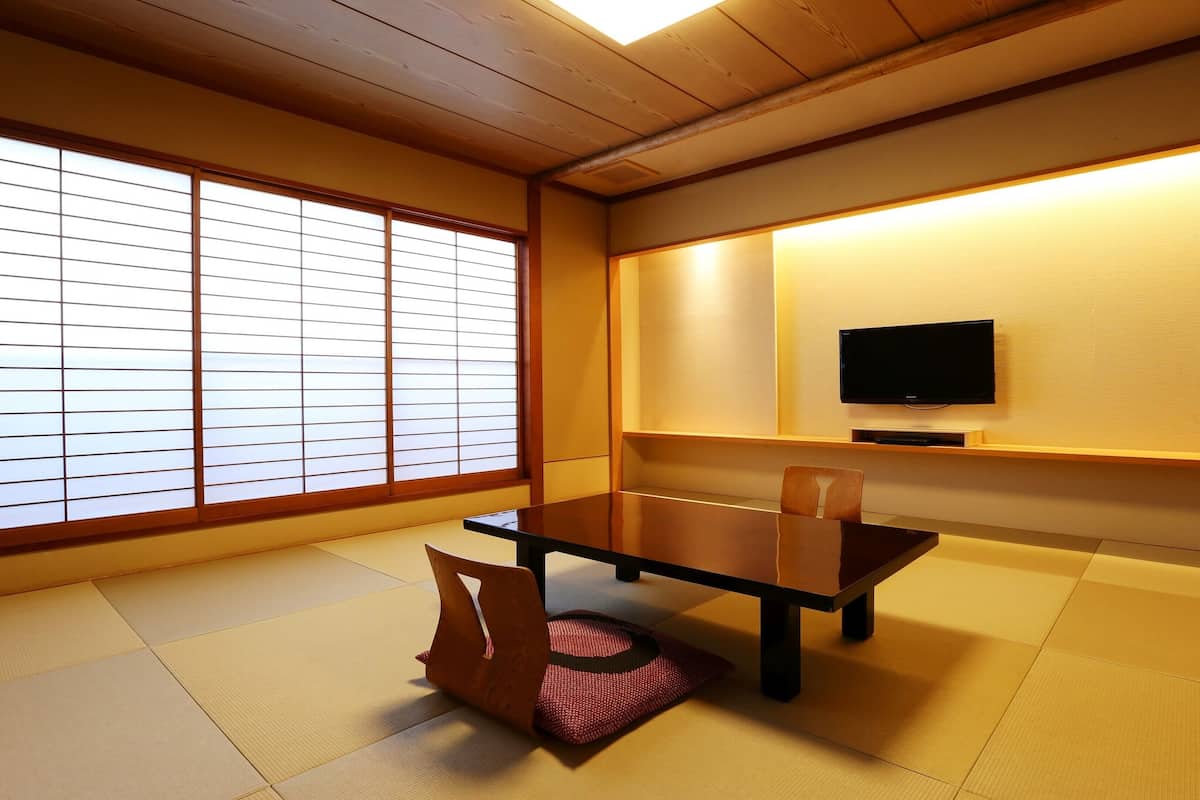 A traditional Japanese room with tatami flooring, a low table, a television, and sliding shoji doors.