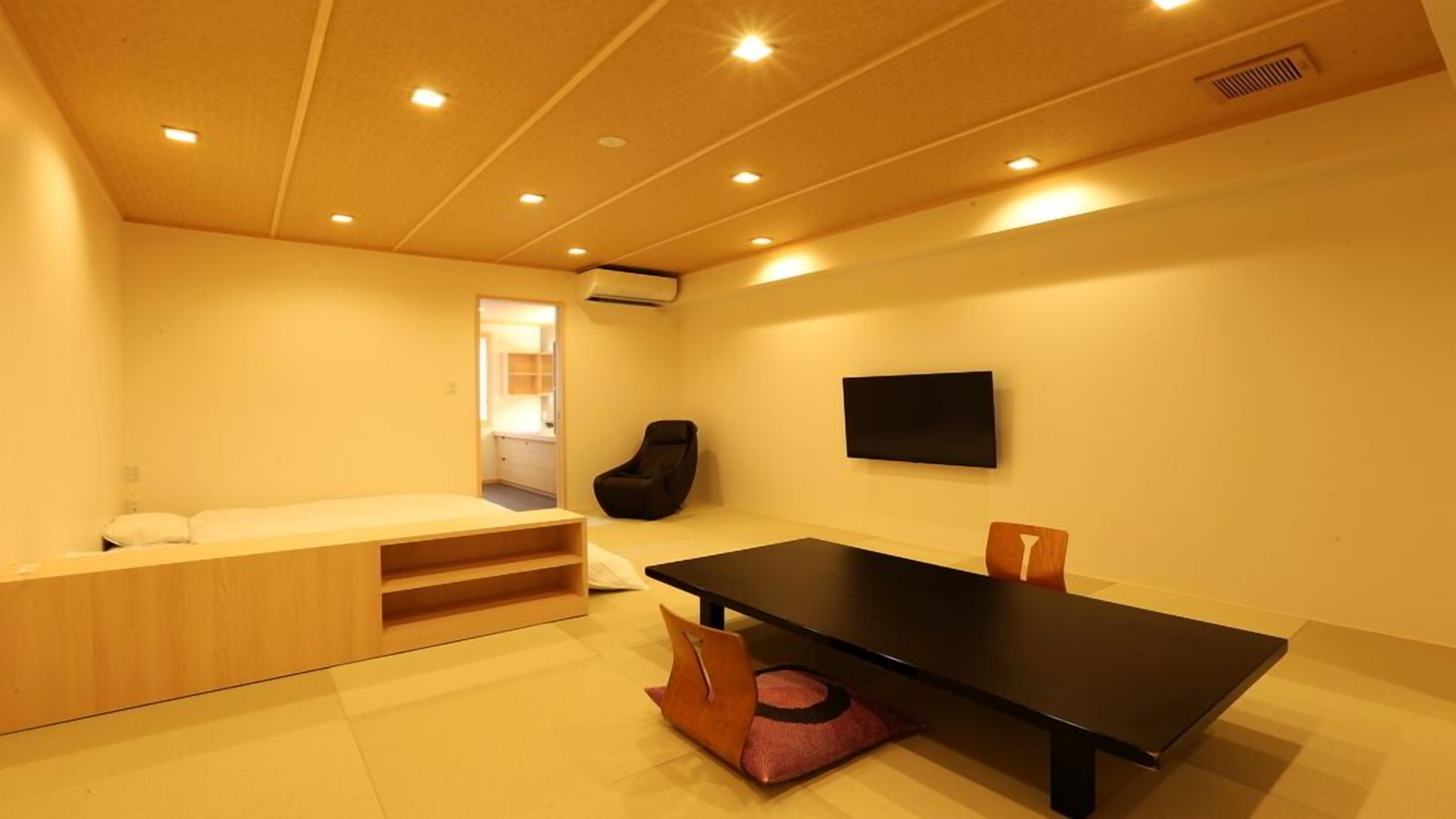 A compact room with a bed, a small seating area, a table, and a chair.
