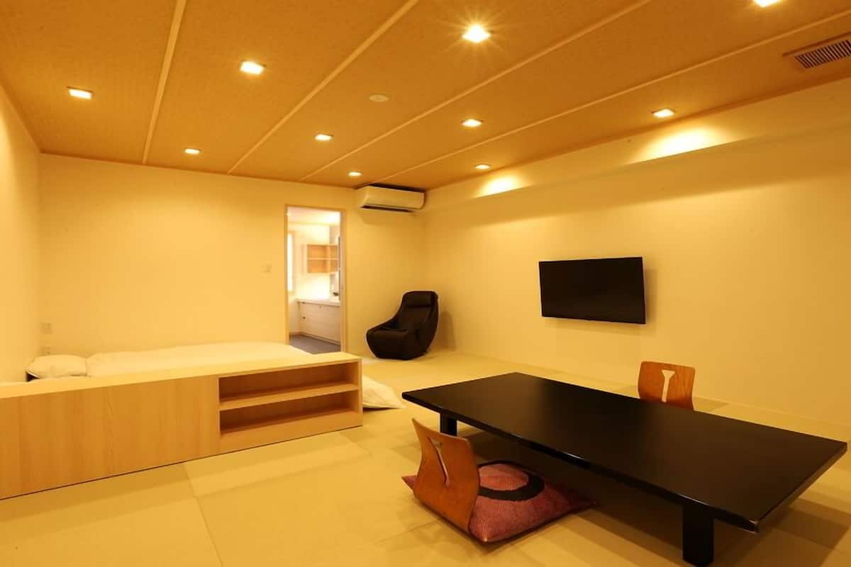 A compact room with a bed, a small seating area, a table, and a chair.