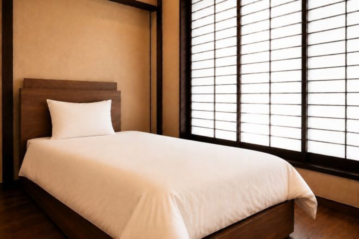 A neatly made bed with a wooden headboard in a room with a large window and blinds.