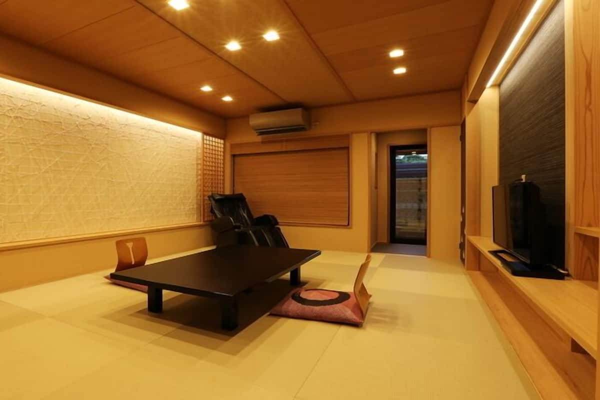 A room with a wooden floor, a black table, a black chair, a television, and a sliding door.