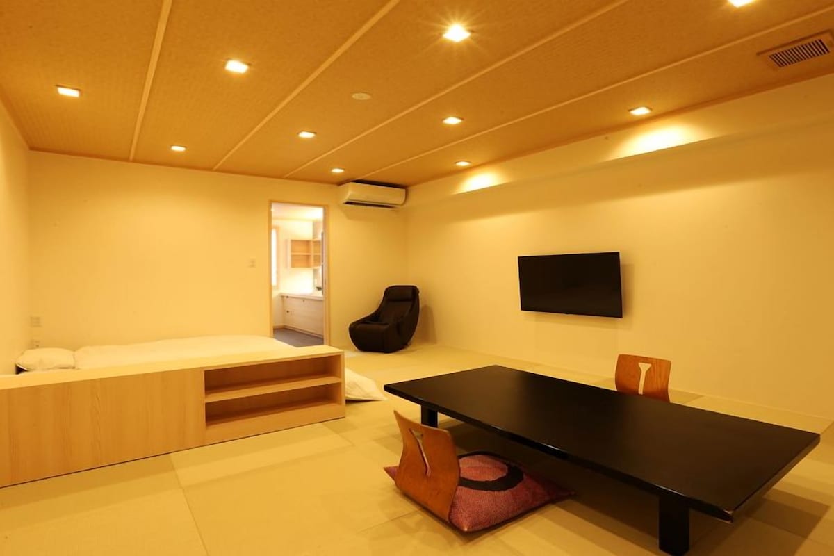 A compact room with a bed, a small seating area, a table, and a chair.