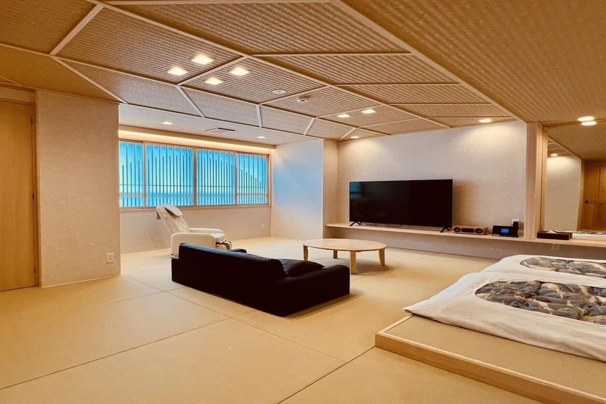 A modern room with a large bed, a TV, a massage chair, and a large window.