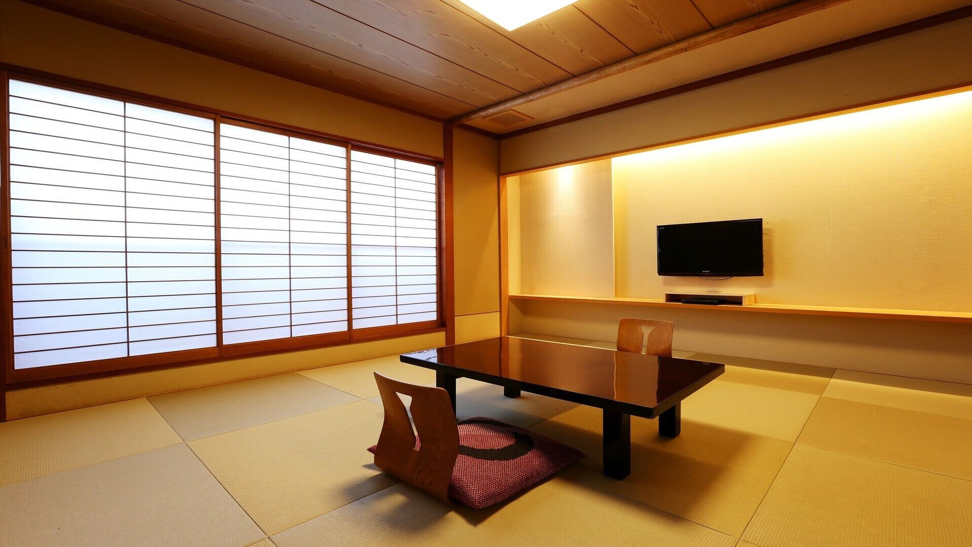 A traditional Japanese room with tatami flooring, a low table, chairs, a television, and sliding shoji doors.