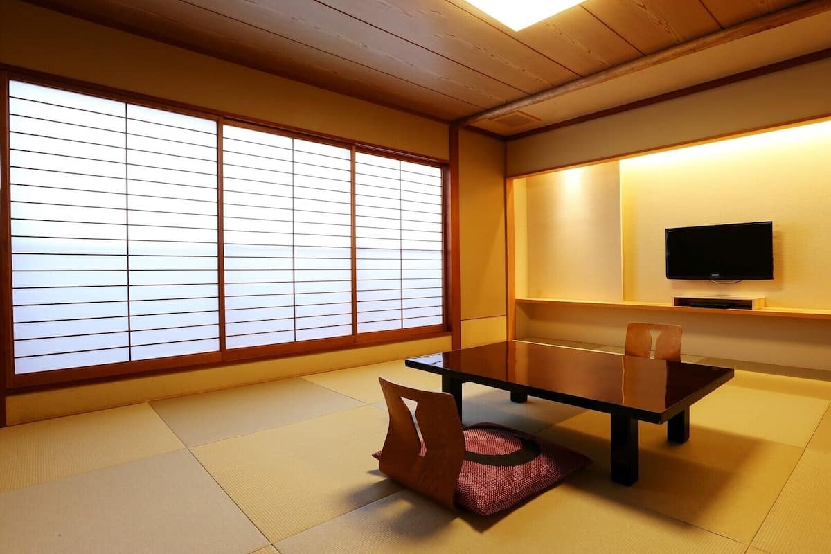 A traditional Japanese room with tatami flooring, a low table, chairs, a television, and sliding shoji doors.