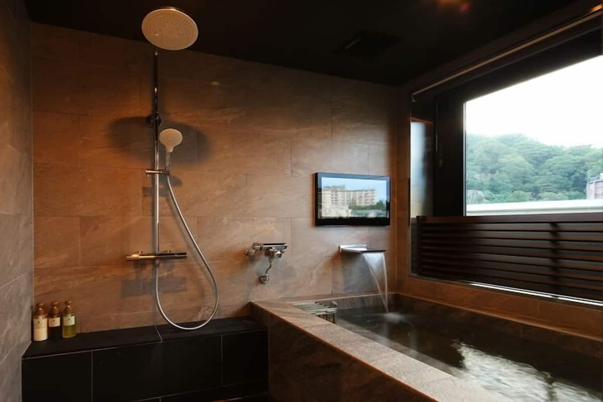 A modern bathroom with a bathtub, a shower, and a window with a view of greenery.
