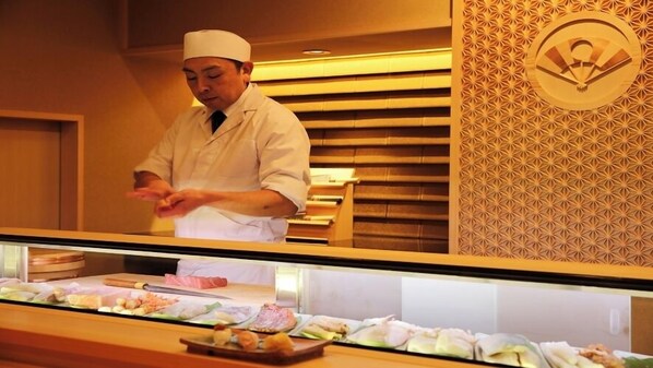 A chef in a white uniform behind a counter with various food items displayed. - Arima Royal Hotel (Kobe)