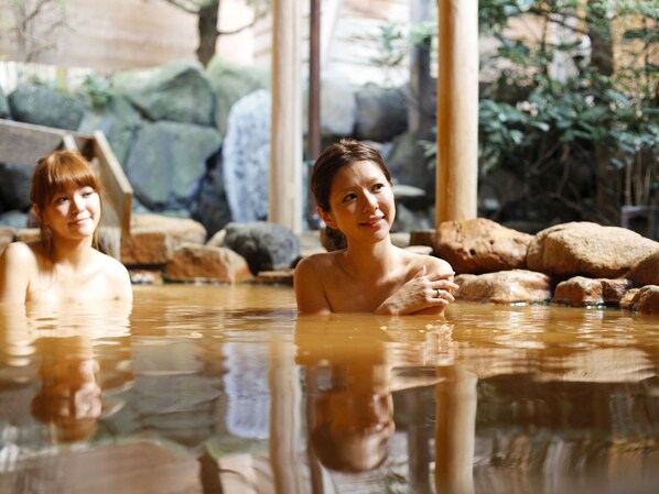 Two people in a hot spring bath surrounded by rocks and greenery.