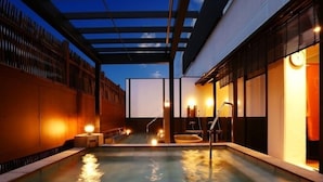 A heated outdoor pool area with a pergola overhead, a small seating area, and a wall with a clock. - Arima Royal Hotel (Kobe)