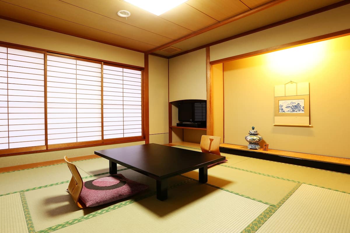 A traditional Japanese room with tatami flooring, a low table, a television, and a decorative vase.