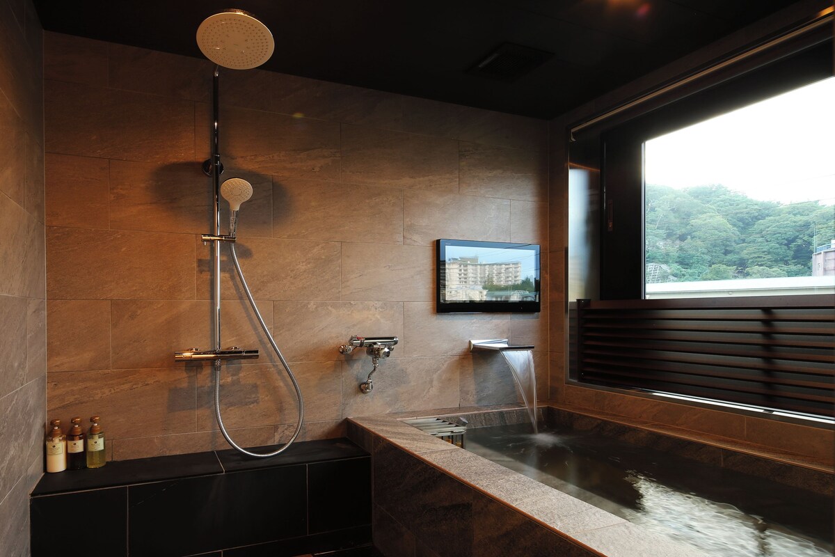 A modern bathroom with a shower, bathtub, and a window with a view of greenery.