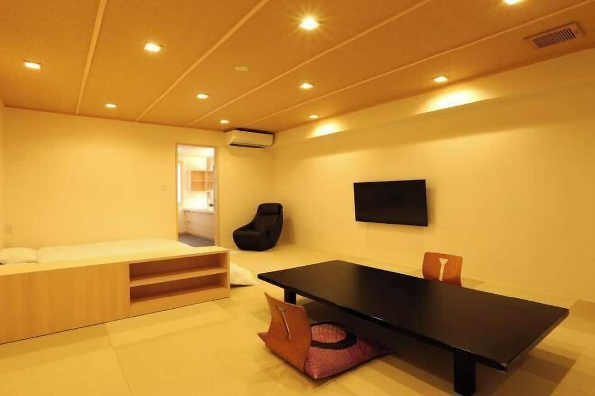 A modern room with a bed, a black table, and a TV on the wall.