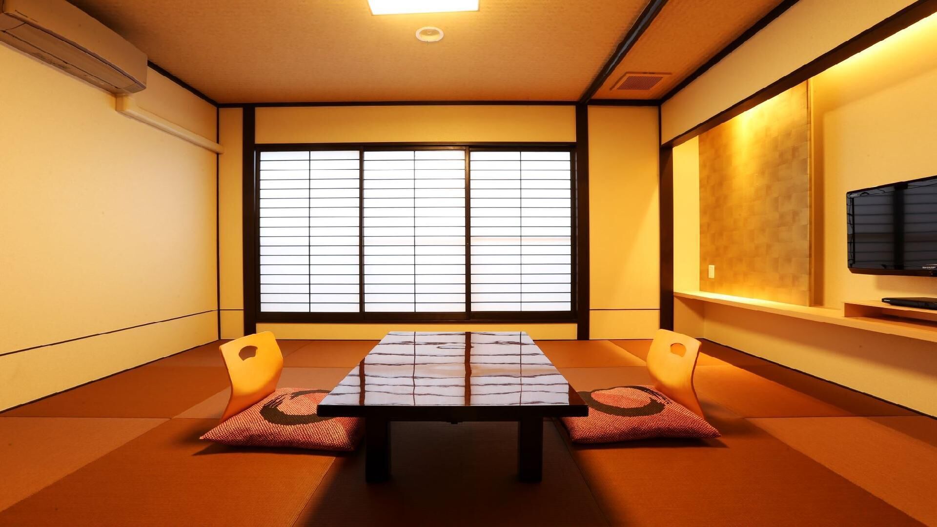 A traditional Japanese room with tatami flooring, a low table, cushions, a sliding shoji screen, and a mounted television.